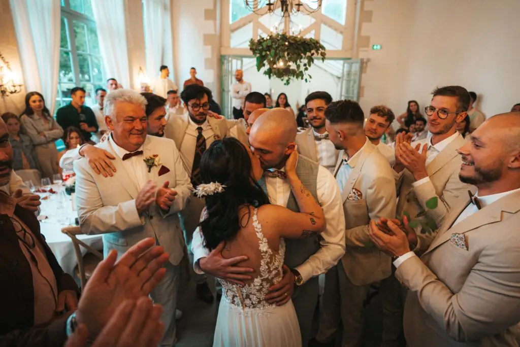 Photo du couple de mariés prise par Weddevent lors de la soirée dansante de leur mariage, s'embrassant au milieu de leurs invités.